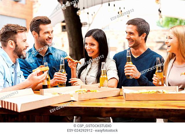 Spending great time with friends. Group of joyful young people eating pizza and drinking beer while standing outdoors