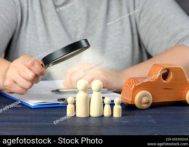 female hand examines wooden figures of the family in a magnifying glass. The concept of studying the credit history of the borrower, reliability