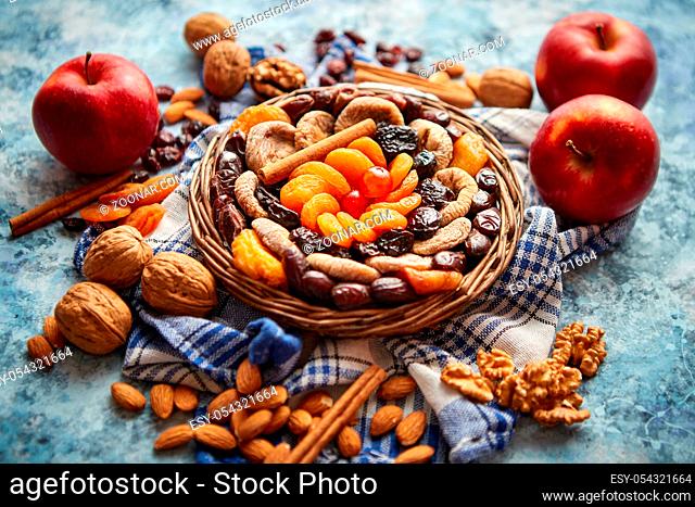 Composition of dried fruits and nuts in small wicker bowl placed on a stone table. Assortment contais almonds, walnuts, apricots, plums, figs, dates, cherries