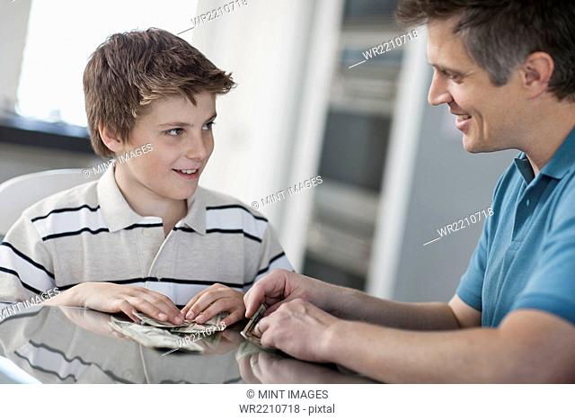 A man and a boy seated at a table, counting and handling cash