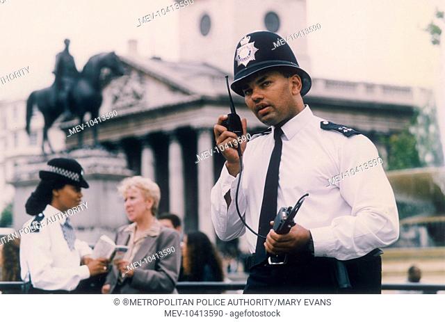 A Metropolitan Police officer speaking on his radio in Trafalgar Square, Central London, with the church of St Martin in the Fields behind him