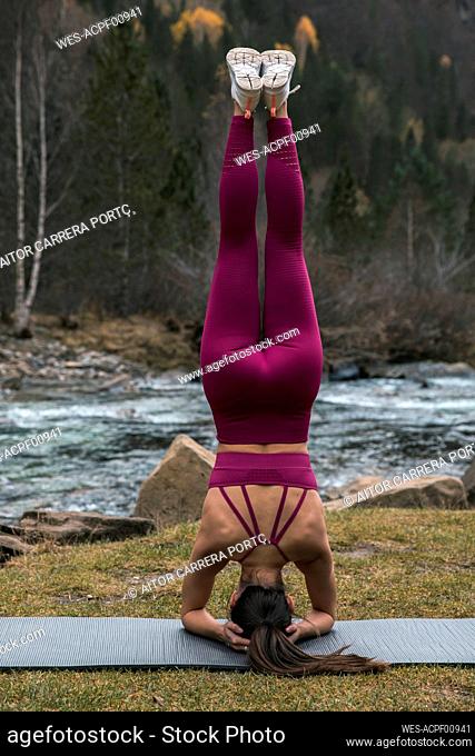 Active young woman practicing headstand pose on yoga mat at Ordesa National Park, Huesca, Spain