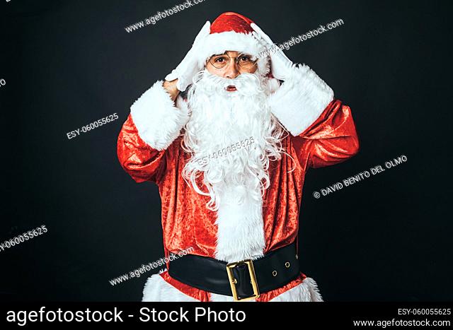 Man dressed as Santa Claus surprised with hands on head, on black background. Christmas concept, Santa Claus, gifts, celebration