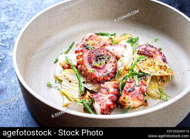 Traditional French octopus braised cooked with chicory and salicornia in wine sauce as closeup on a modern design bowl