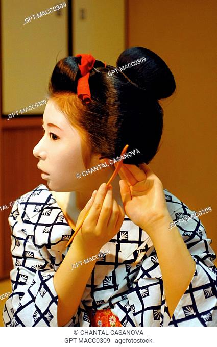THE MAIKO’S APPRENTICE GEISHA TRADITIONAL HAIRDO. A MAIKO ARRANGING HER CHIGNON IN THE FORM OF A PEACH WARESHINOBU ADORNED WITH SILK RIBBONS KANOKO WITH A COMB...
