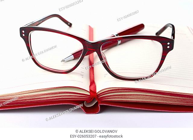 Red Daily planner with eyeglasses and pen, closeup