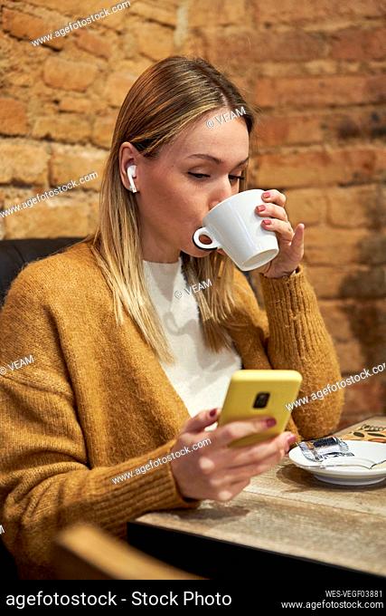 Young woman drinking coffee while using mobile phone in cafeteria