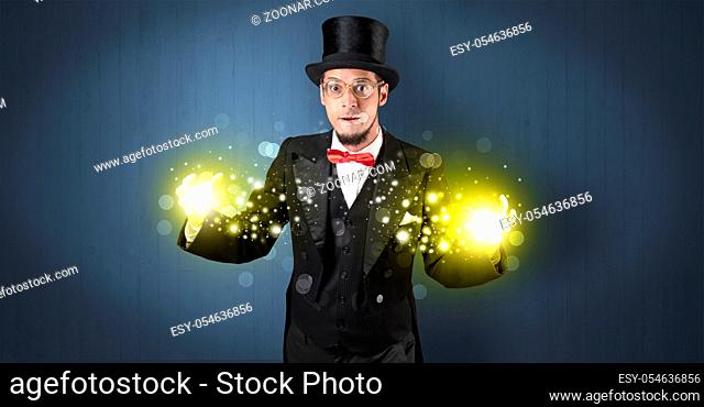Handsome illusionist holding his superpower on his hands with gold wallpaper
