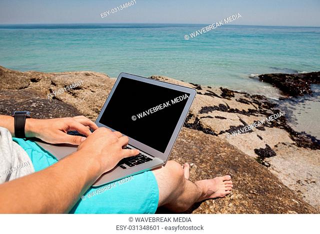 Man sitting on the rocks and using laptop at the sea coast