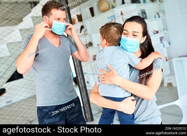 Eltern und Kleinkind mit Mund-Nasen-Schutz gegen Covid-19 im Wohnzimmer