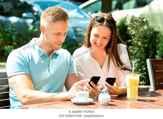 Young Happy Couple Sitting On Bench Using Mobile Phone