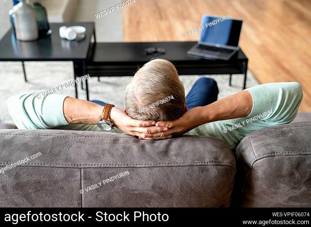 Man with hands behind head sitting on sofa at home