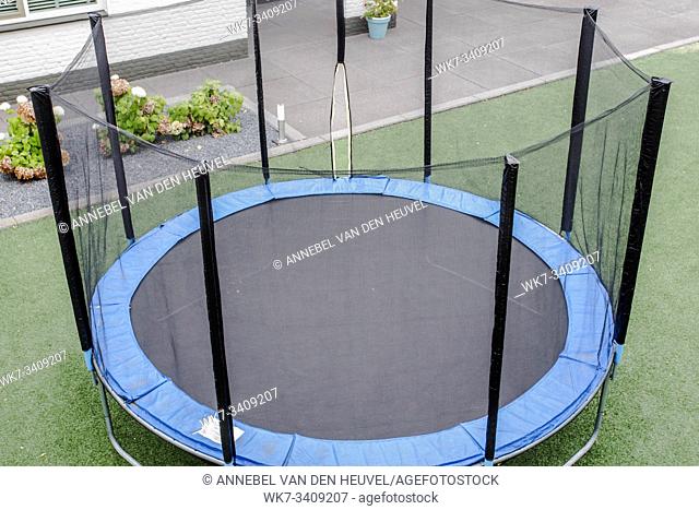 Blue trampoline with safety net on the lawn in garden outdoors for children