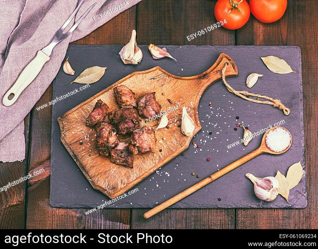 pieces of fried pork on a brown wooden board with spices, top view