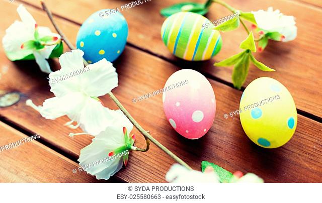easter, holidays, spring, tradition and object concept - close up of colored easter eggs and flowers on wooden surface