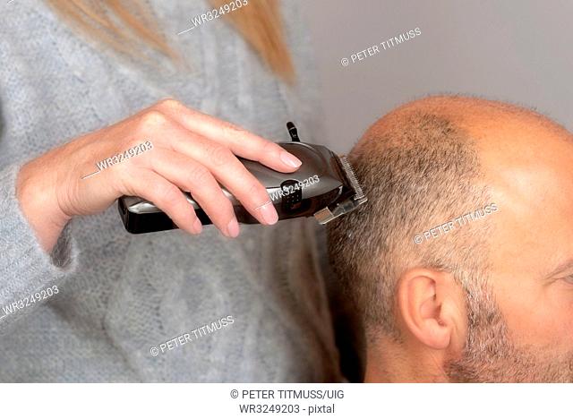 Portable electric hair clippers being used to give a balding man a crew cut hair style