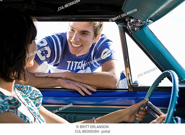 Man leaning into car smiling at woman