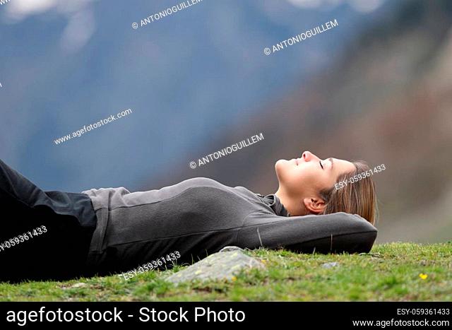 Side view portrait of a relaxed trekker resting lying on the grass in the mountain