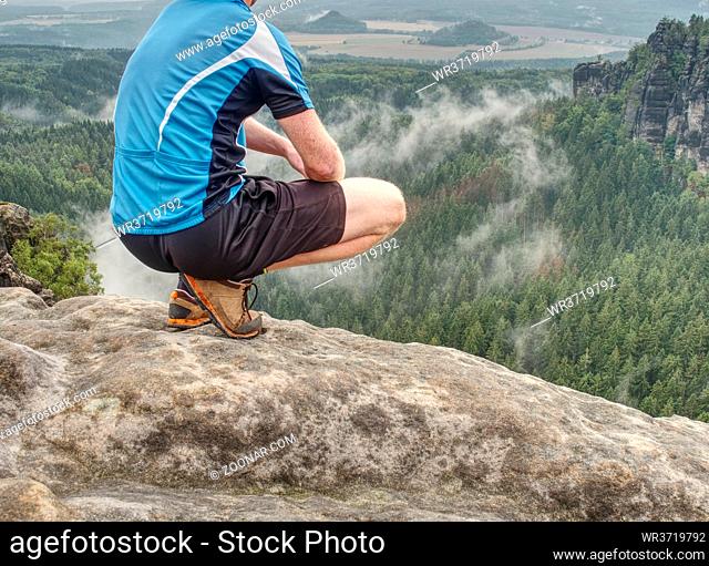 Hiker legs hiking in fall nature. Guy just relax on mountain top and enjoy view. Feets in trekking shoes and legs short running trousers