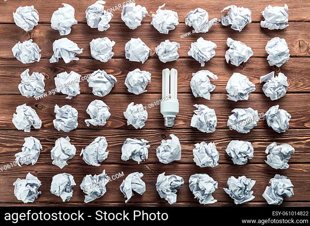 Incandescent bulb and crumpled white paper balls on brown wooden table