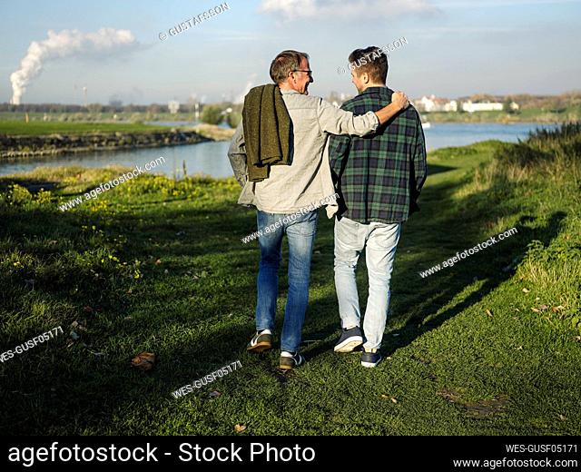 Father arm around son walking at riverbank