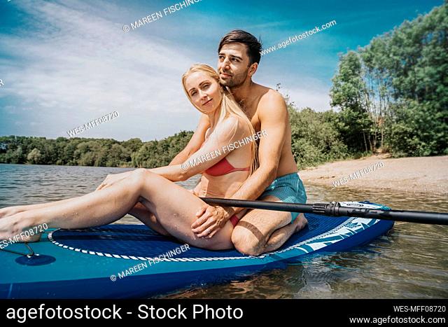 Thoughtful man with woman sitting on paddleboard at weekend