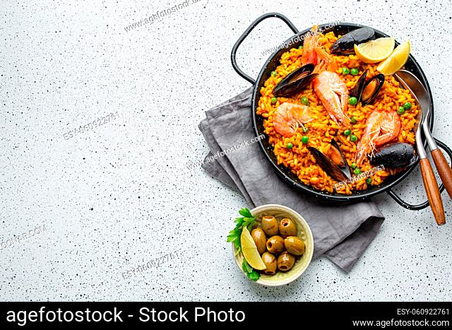 Classic dish of Spain, seafood paella in traditional pan on white wooden background top view. Spanish paella with shrimps, clamps, mussels