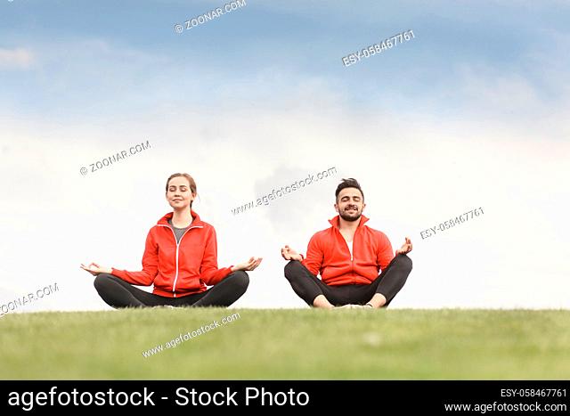 Evening yoga on background of beautiful sky. Man and woman meditating in mountains. People relax at sunset