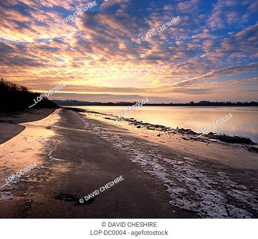 England, Gloucestershire, Westbury-on-Severn, A dawn sky is reflected in the water and icy shore of the River Severn