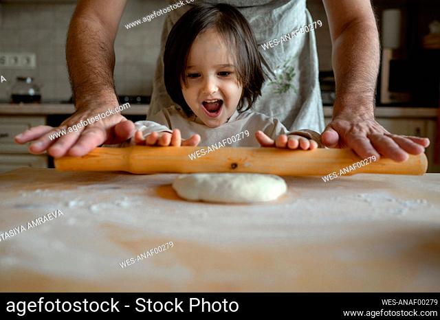 Happy boy with father rolling pizza dough in kitchen