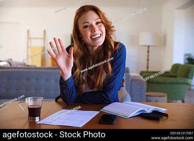 Portrait of woman waving while sitting on her desk at home