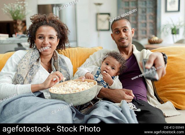 Happy couple with baby daughter watching TV and eating popcorn
