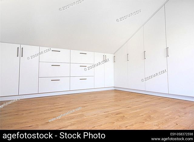 Modern white built-in wardrobe in empty room with sloping ceiling