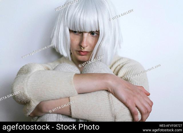 Woman hugging knees in front of wall
