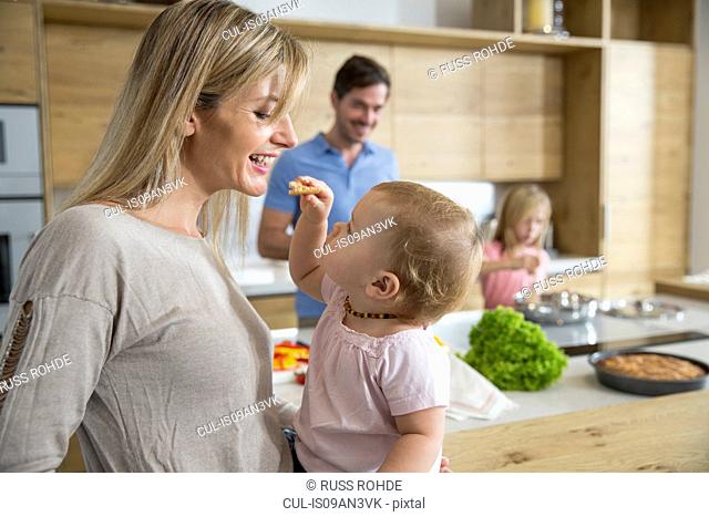 Female toddler feeding mother in kitchen