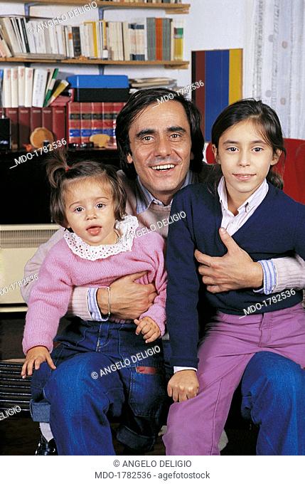 Roberto Vecchioni with his daughters. Italian singer-songwriter and writer Roberto Vecchioni smiling with his daughters Carolina and Francesca on his knee