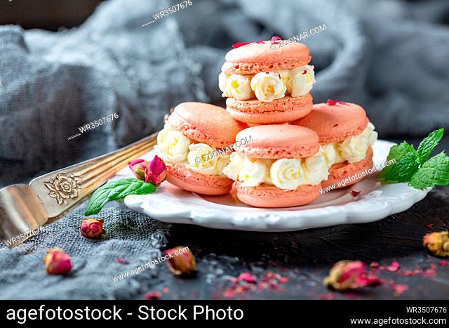 Plate of macarons with white cream roses, green mint and pink buds on a dark background, selective focus