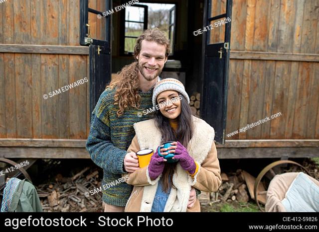 Portrait happy young couple drinking coffee outside tiny cabin rental