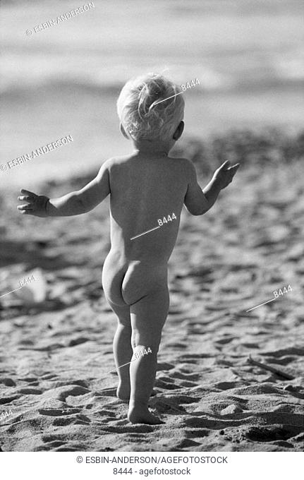 Nude toddler boy running on beach