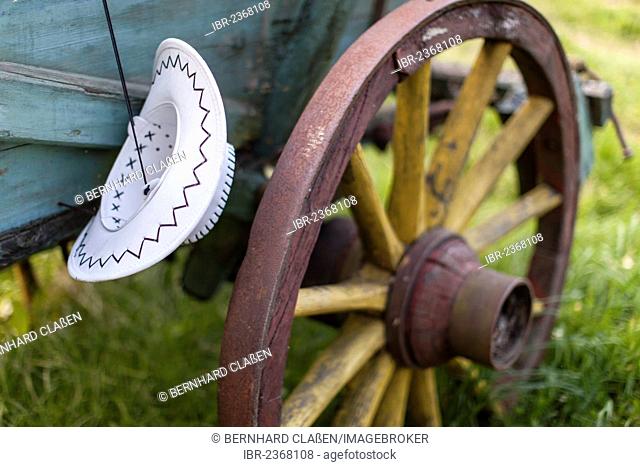 Cowboy hat hanging on a horse trailer, wooden spoked wheel