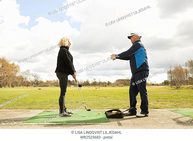 Man assisting woman in playing golf at driving range
