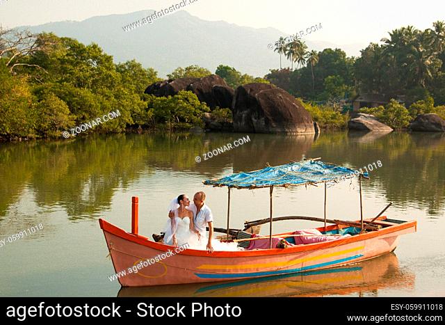Love story on the lake in a wooden boat, a man in a white shirt and a beautiful girl in a wedding dress