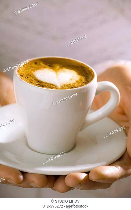 Woman holding cup of espresso macchiato with milk foam heart