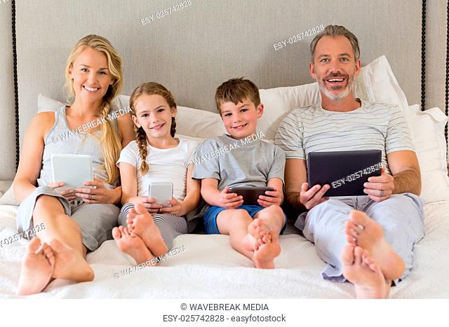 Parents and kids using mobile phone and digital tablet on bed
