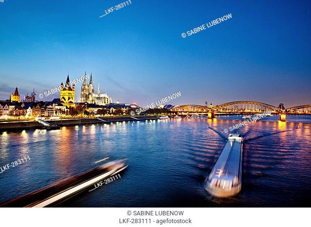 View over river Rhine to old town with cathedral and Great St. Martin church at night, Cologne, North Rhine-Westphalia, Germany