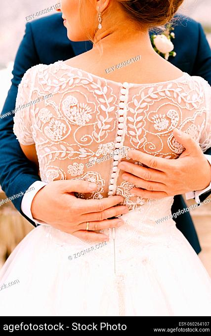 The bride and groom are standing and hugging, hands of the groom on bride's back, close-up. High quality photo