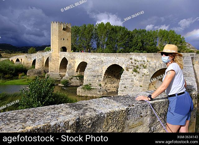 Tourist woman with a hat and a mask and medieval bridge and Ebro river. Frias town. Burgos province. Castile and Leon, Spain