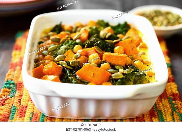 Baked pumpkin, kale and chickpea casserole with pumpkin seeds on top in casserole dish, photographed with natural light (Selective Focus
