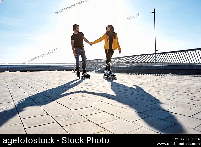 Young couple looking at each other while roller skating on pier during sunny day