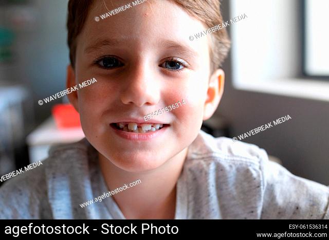 Close-up portrait of smiling elementary schoolboy sitting at desk in classroom